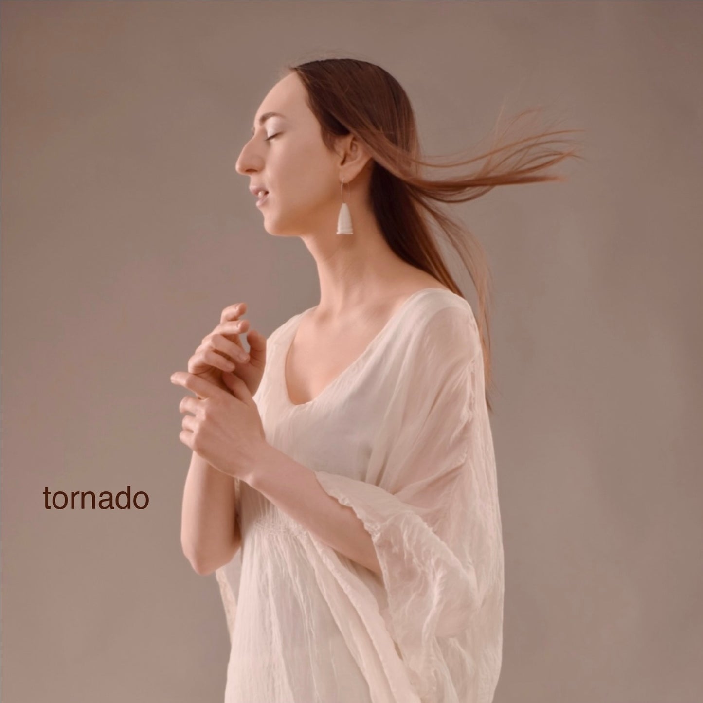 A woman in a flowing white dress wearing the ‘Tornado’ porcelain earring by Serhiy Verbicki, her hair caught in motion, evoking elegance and serenity.